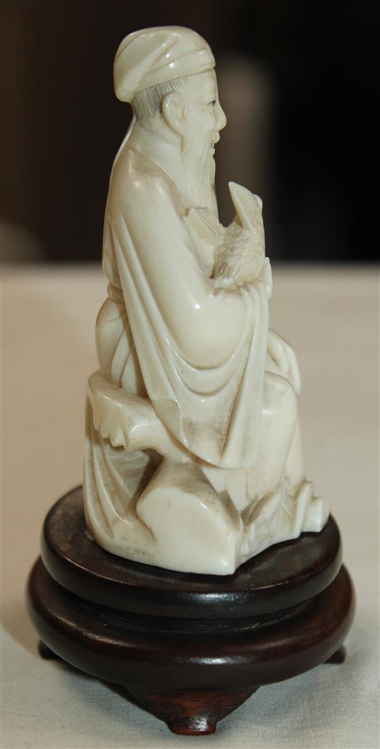 A Chinese ivory seated figure of a scholar holding a bird, early 20th century, wood stand, total height, 10cm